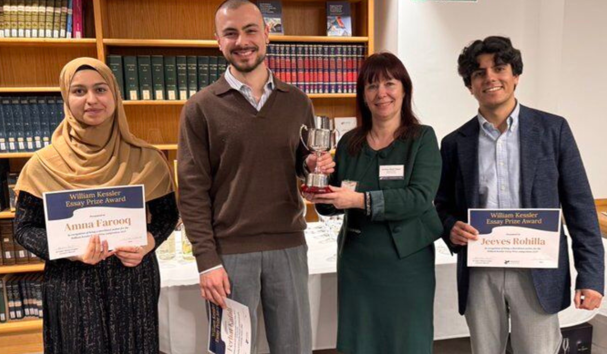 A photograph of four people standing in front of a bookshelf filled with legal or academic books in a formal setting. 