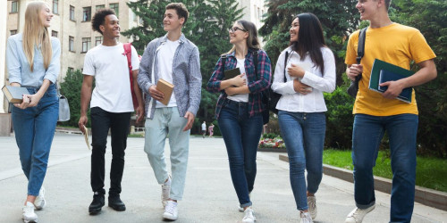 Mixed group of six students walking and talking on university campus