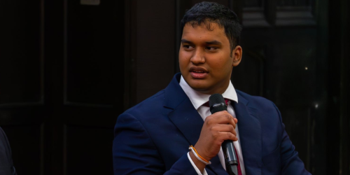 Damsith during a talk. He is holding a microphone and waering a blue suit and white shirt